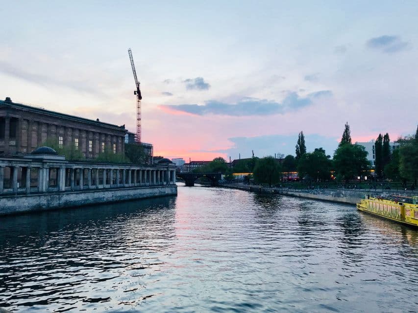Un ampio fiume cittadino al tramonto, con un edificio classico e una gru da cantiere su una sponda e una barca gialla sull'altra.