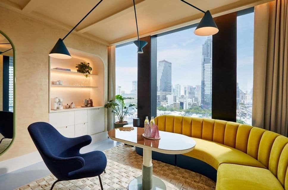 Un espace repas moderne doté d'un canapé jaune incurvé et d'un fauteuil bleu, offrant une vue imprenable sur la ville à travers une grande baie vitrée.