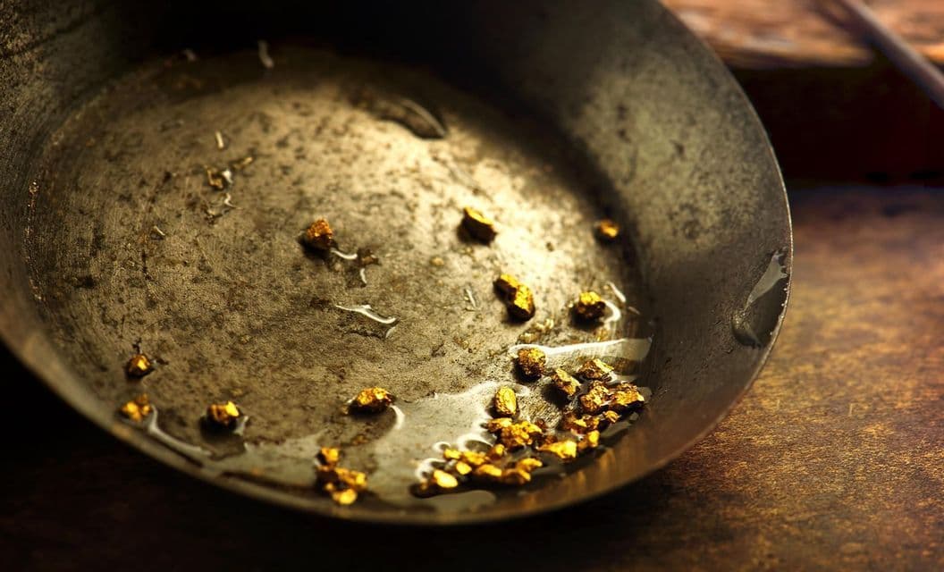 Primo piano di pepite d'oro e gocce d'acqua in una rustica batea da minatore.