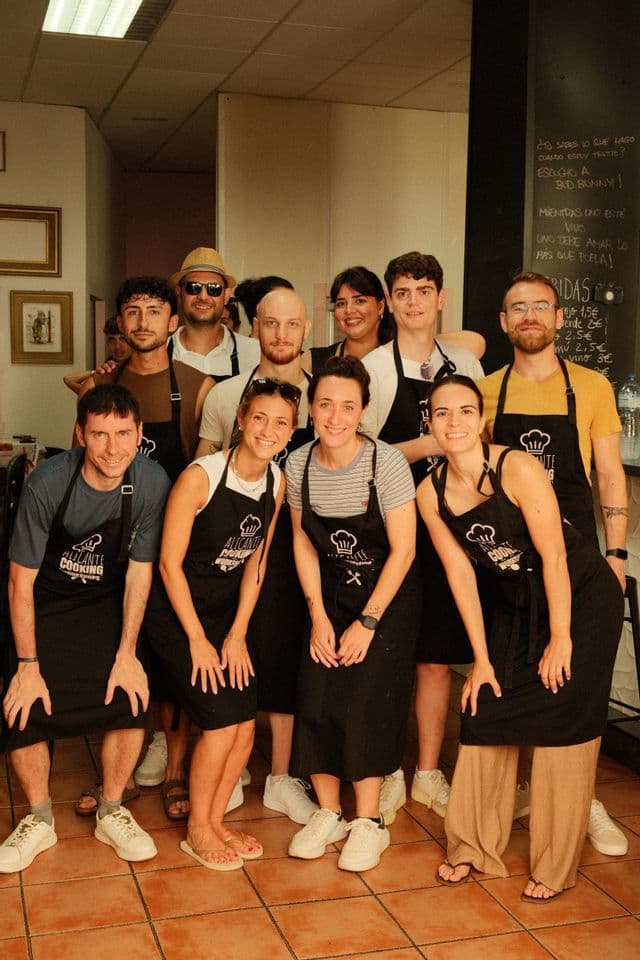 Un gruppo WeRoad in posa per una foto con grembiuli neri abbinati durante una lezione di cucina.