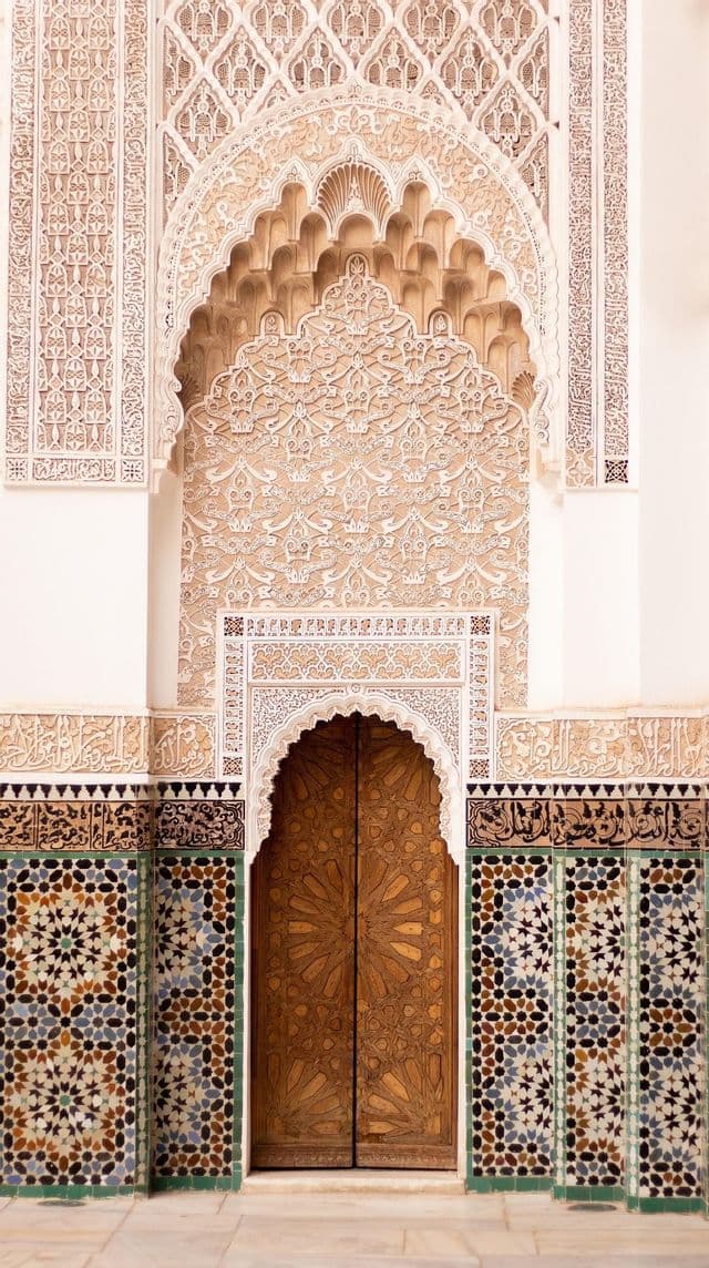 Una puerta de madera ornamentada bajo un arco decorativo con tallas intrincadas y azulejos de mosaico coloridos en la pared.