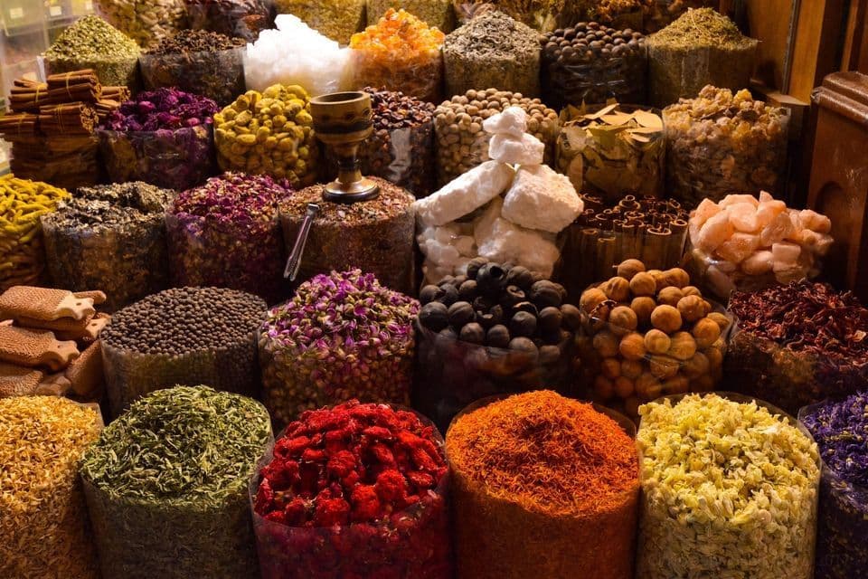 Un surtido colorido de especias, flores secas y hierbas exhibidas en grandes recipientes abiertos en un puesto de mercado.
