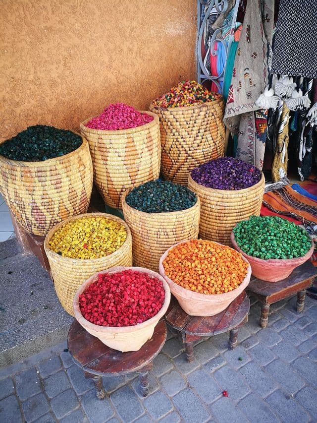 Flores secas coloridas y popurrí exhibidos en cestas tejidas y cuencos de terracota en una calle adoquinada.