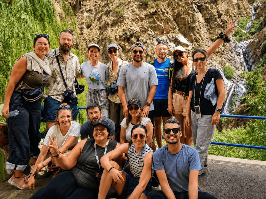 Un grupo de WeRoad sonriendo y posando para una foto frente a una montaña rocosa y una cascada.