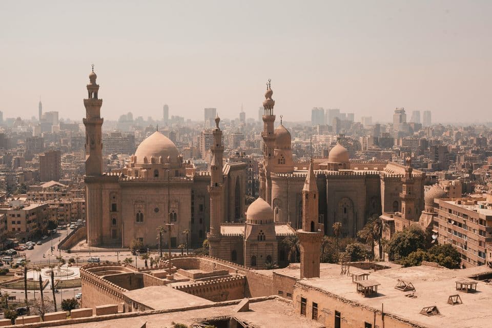 Vue panoramique de plusieurs grandes mosquées avec dômes et minarets, sur fond de skyline urbaine moderne et brumeuse.