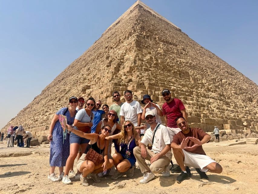 Un groupe WeRoad en voyage pose pour une photo de groupe devant une grande pyramide de pierre sous un ciel dégagé.