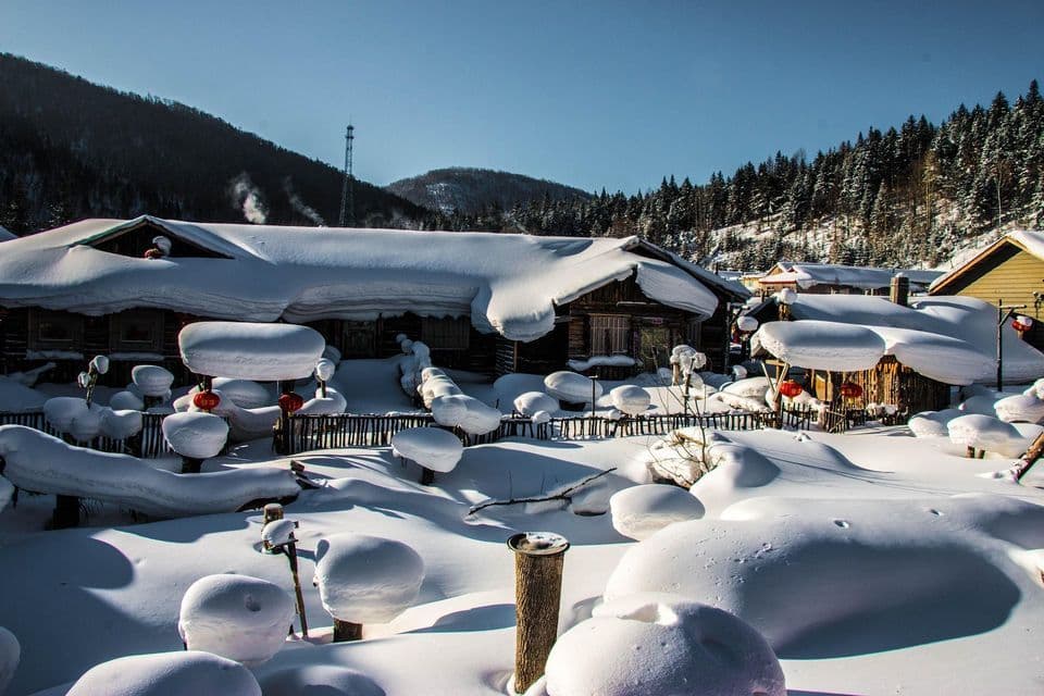 Cabañas de madera en un pueblo de montaña cubierto por una gruesa capa de nieve bajo un cielo azul despejado.