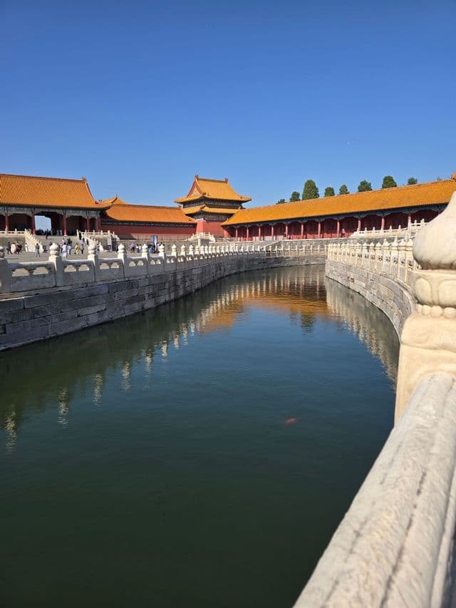 Un fossato curvo riflette gli edifici tradizionali asiatici con tetti di tegole arancioni sotto un cielo azzurro e limpido.