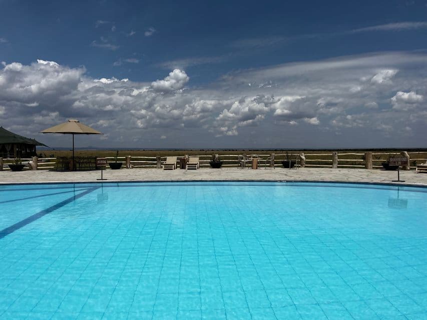 Ein blauer Pool mit Liegestühlen auf einer Terrasse blickt auf eine grasbewachsene Ebene unter einem teilweise bewölkten Himmel.