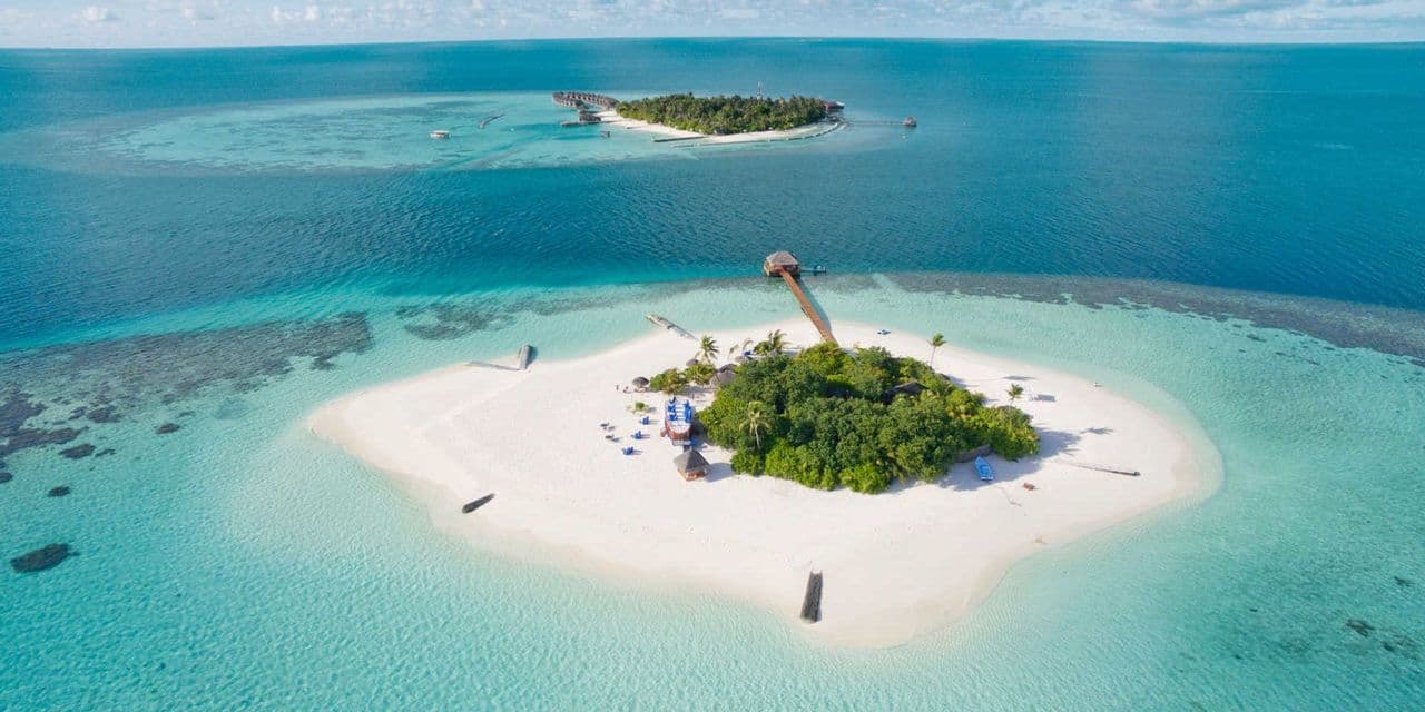 An aerial view of two small tropical islands with white sand beaches and lush greenery, set in a turquoise and deep blue ocean.