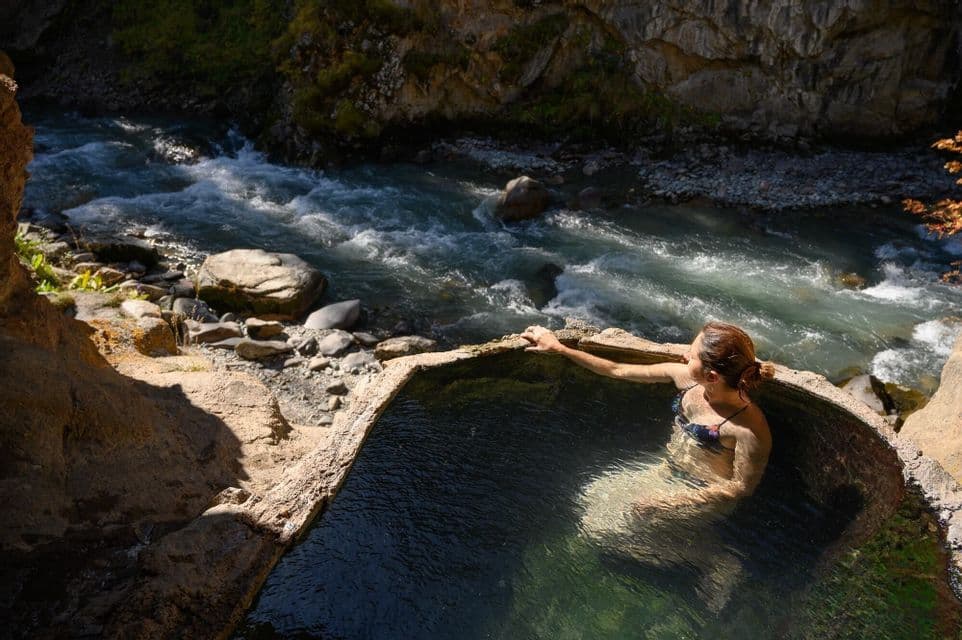 Una donna si rilassa in una sorgente termale naturale scavata nella roccia, che domina un fiume impetuoso in un canyon.