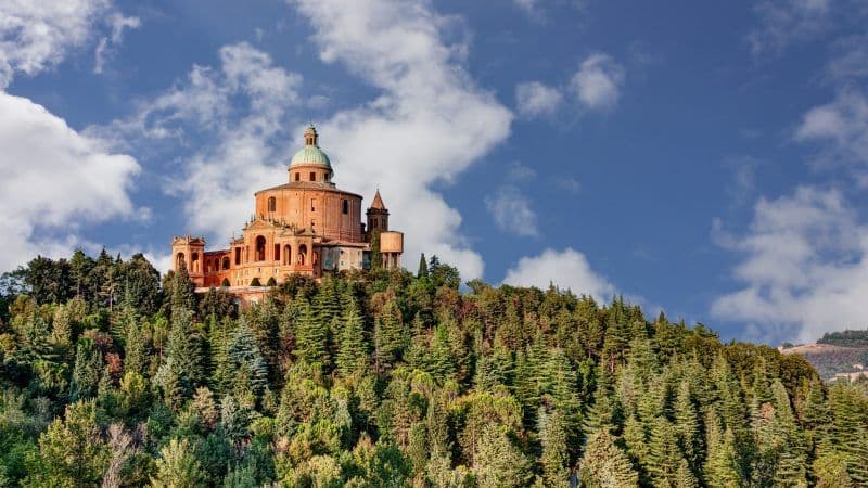 Un grande santuario a cupola si erge su una collina boscosa sotto un cielo azzurro con nuvole bianche.
