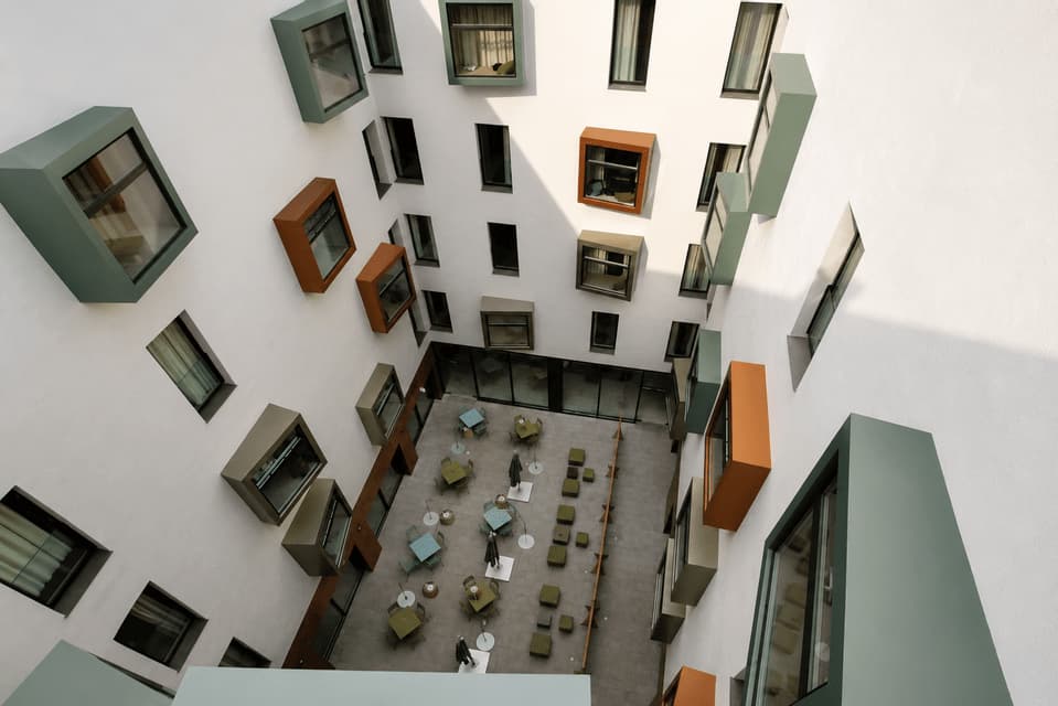 Vista dall'alto di un cortile interno di un edificio moderno, con finestre geometriche e multicolori che sporgono dalle pareti bianche.