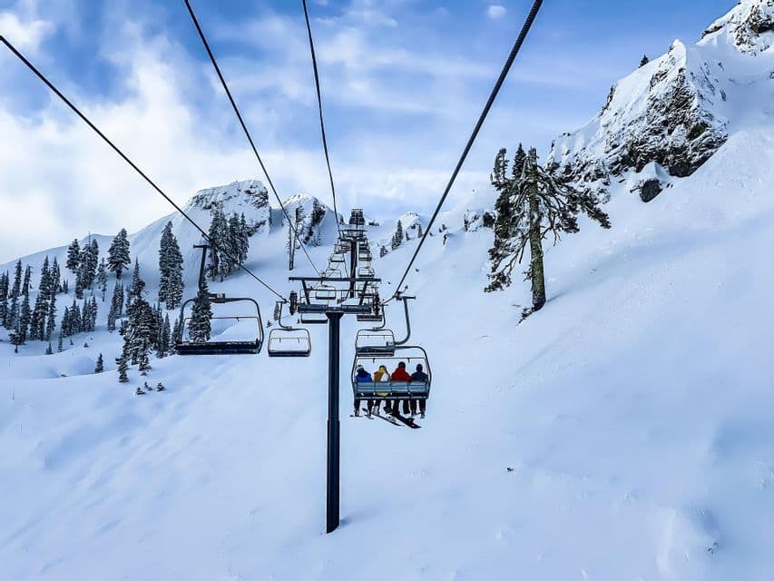 Un viaggio di gruppo WeRoad su una seggiovia che sale su una montagna innevata con pini sotto un cielo parzialmente nuvoloso.