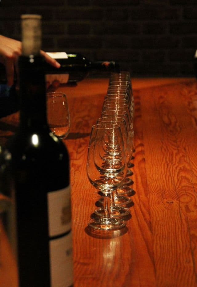 Una persona versa vino rosso in una lunga fila di calici disposti su un tavolo di legno per una degustazione di vini.