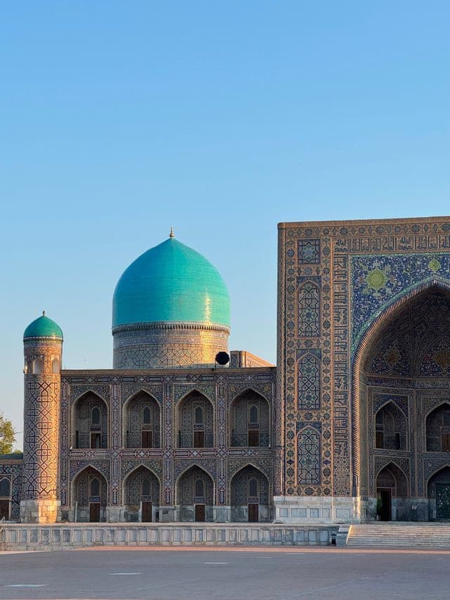 Esterno di un edificio storico con cupole turchesi e mura a mosaico dettagliate, sotto un cielo azzurro sereno.