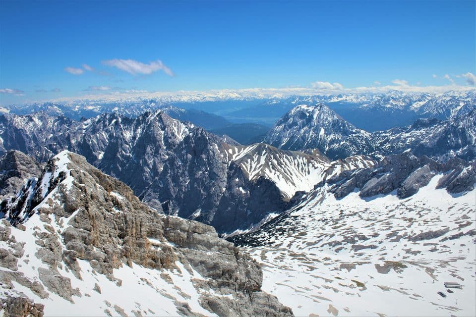 Eine weite, schneebedeckte Bergkette mit felsigen Gipfeln erstreckt sich unter einem klaren blauen Himmel.