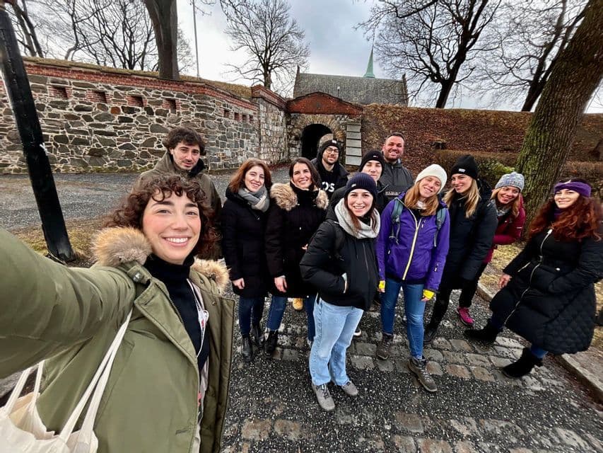 A WeRoad group trip takes a smiling selfie on a cobblestone path in front of an old stone gatehouse.