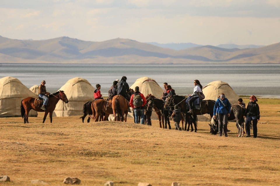 A WeRoad group trip on horseback and on foot in front of a yurt camp with a lake and mountains in the background.