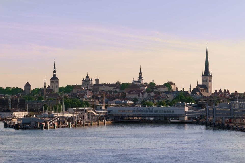Skyline storico della città con guglie e torri di chiese in evidenza, visto dall'acqua, con un moderno porto in primo piano.