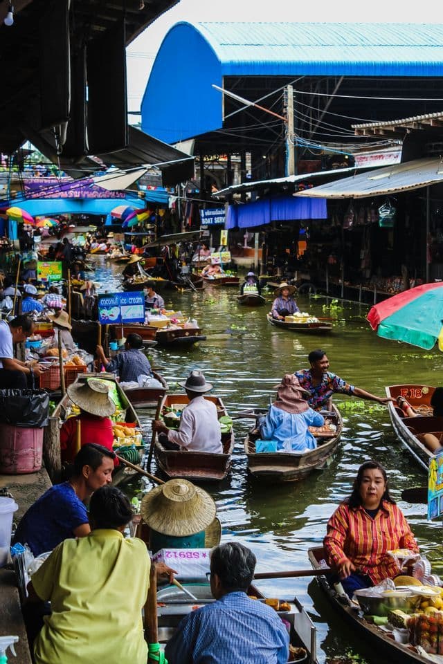 Una vista dall'alto di un vivace mercato galleggiante, con persone su piccole barche di legno che comprano e vendono cibo su un affollato corso d'acqua.