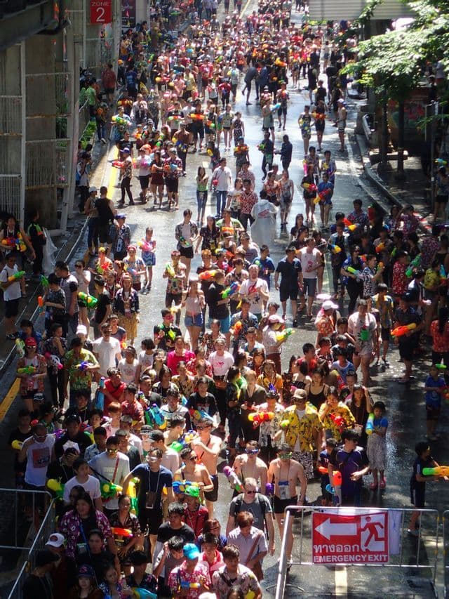 Una vista dall'alto di un'enorme folla di persone con pistole ad acqua colorate che camminano lungo una strada bagnata durante un festival.