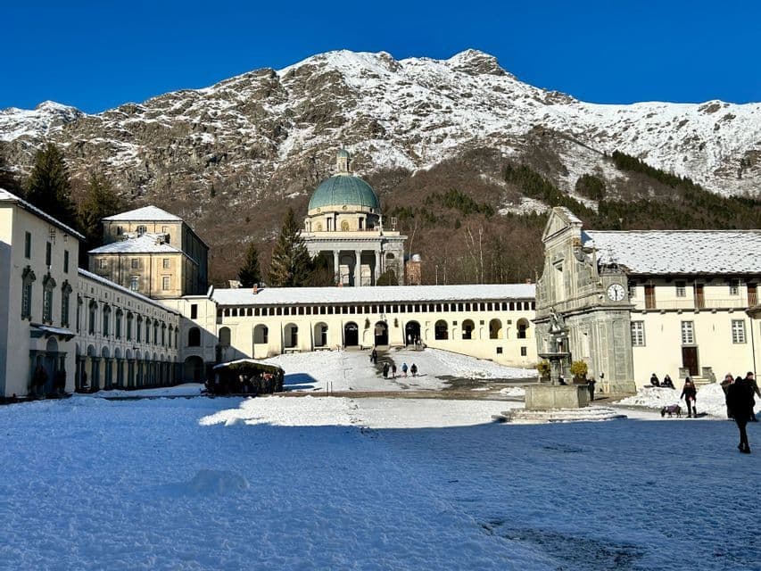 Un vasto complesso di santuari nella neve, con una basilica dalla cupola verde sullo sfondo di un'imponente montagna innevata sotto un cielo limpido.