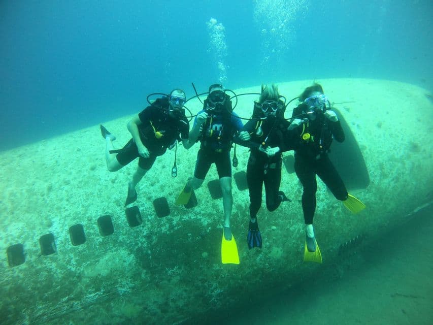 Eine WeRoad-Gruppenreise mit vier Tauchern, die unter Wasser neben einem versunkenen Flugzeugwrack posieren