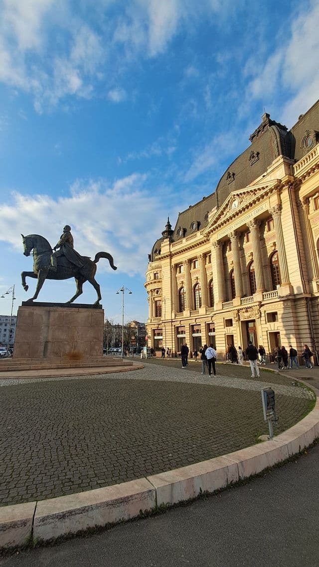 Ein Reiterstandbild steht auf einem gepflasterten öffentlichen Platz vor einem grandiosen neoklassizistischen Gebäude unter einem leicht bewölkten Himmel.