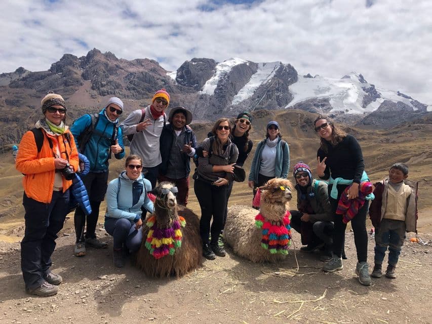 A WeRoad group trip poses for a photo with two decorated llamas in front of a snow-capped mountain range.