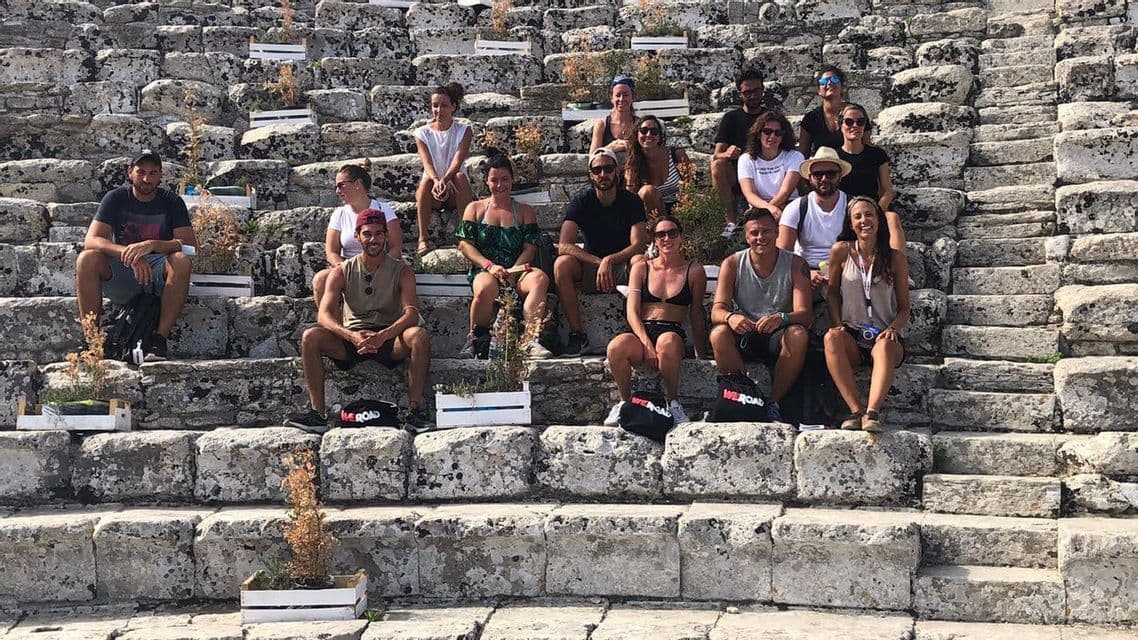 Un groupe WeRoad en voyage posant pour une photo assis sur les larges marches en pierre d'un ancien amphithéâtre.