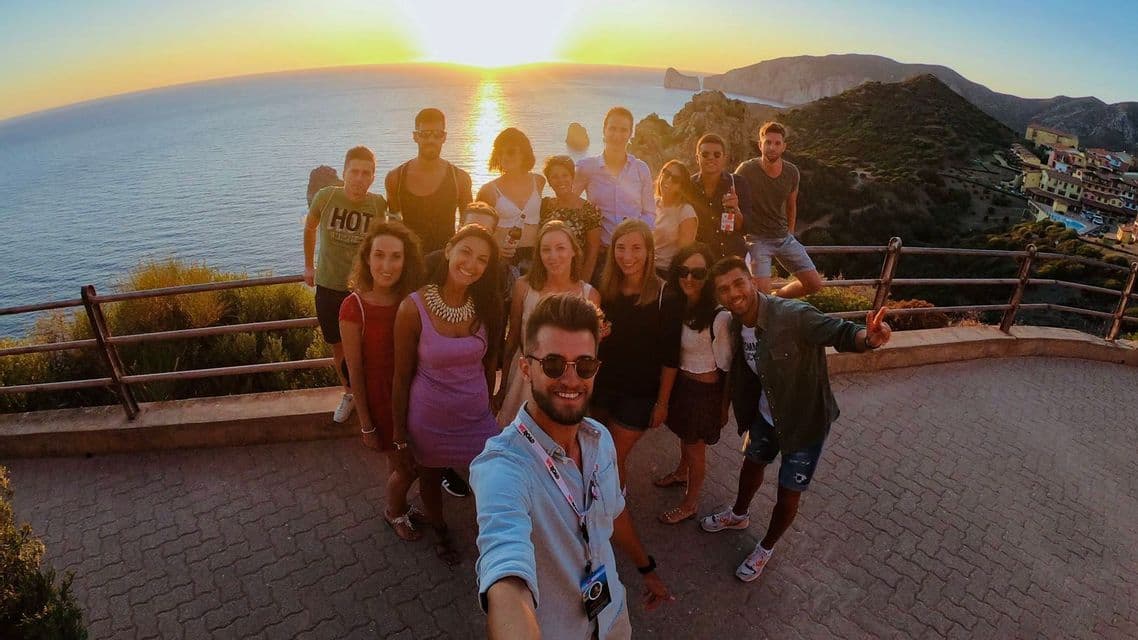 Un gruppo WeRoad in viaggio che posa per un selfie su un punto panoramico con vista mare al tramonto.