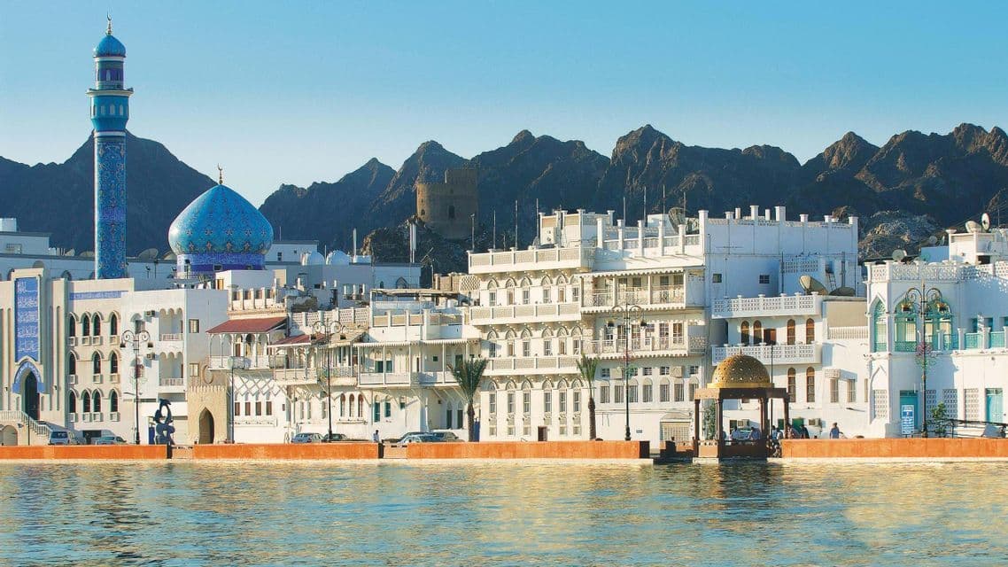 Una città di edifici bianchi, con una moschea dalla cupola blu e un minareto, sorge su un lungomare incorniciato dalle montagne.