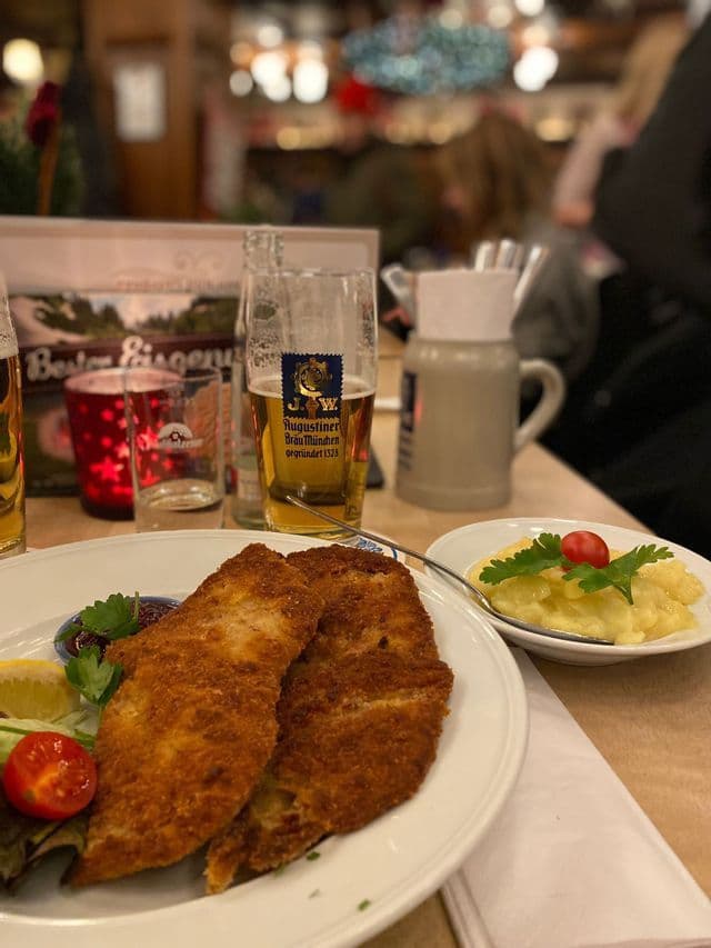 Una cotoletta impanata con insalata di patate e un bicchiere di birra Augustiner su un tavolo da ristorante.