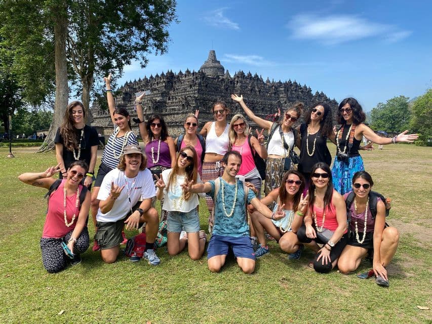 A WeRoad group trip posing for a photo on a grassy lawn in front of an ancient stone temple.