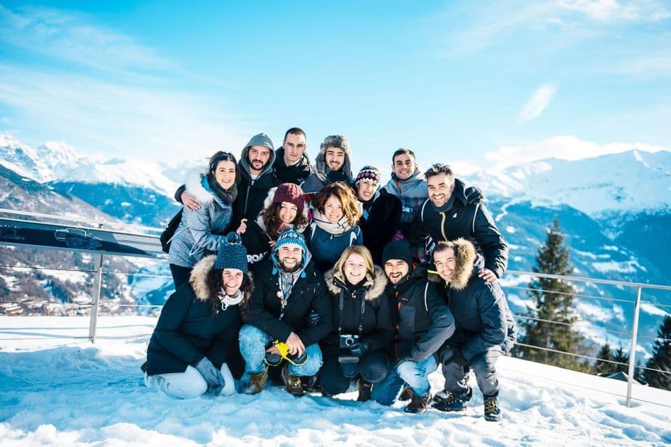 Eine WeRoad-Gruppenreise posiert für ein Foto auf einem verschneiten Berg unter einem sonnigen, klaren Himmel.