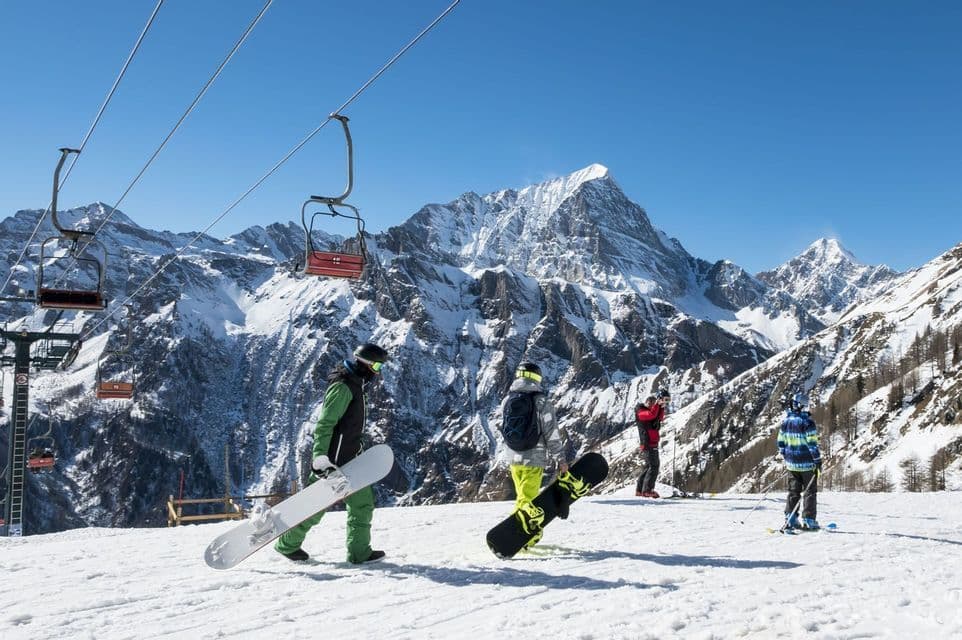 Eine WeRoad-Gruppenreise mit Snowboardern auf einem verschneiten Hang, mit einem Sessellift und Bergen im Hintergrund.
