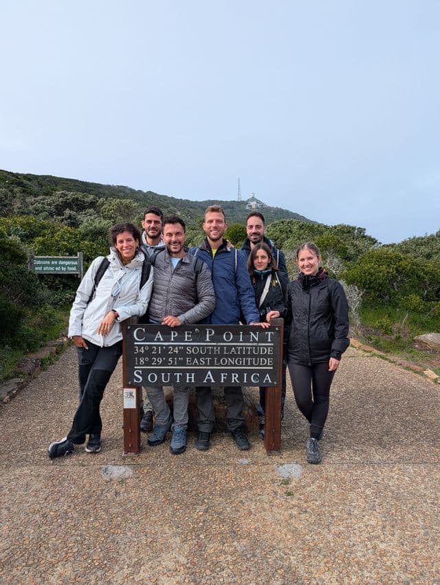 Eine WeRoad-Gruppe von Reisenden posiert gemeinsam hinter einem hölzernen Wegweiser an einem asphaltierten Wanderweg.