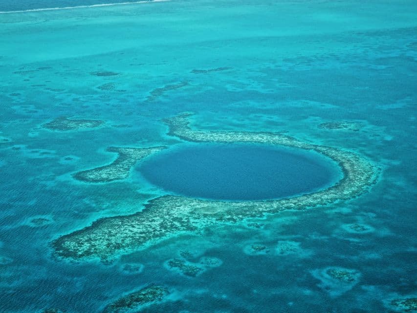 Eine Luftaufnahme eines großen, kreisförmigen blauen Lochs, umgeben von einem türkisfarbenen Korallenriff mitten im Ozean.