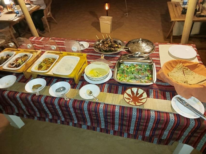 Buffet cena all'aperto con spiedini, insalata e focaccia, allestito su un lungo tavolo con tovaglia a fantasia.