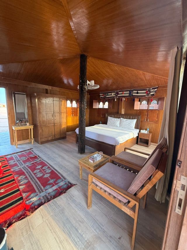 L'interno di una spaziosa tenda-camera con pannelli in legno, dotata di un letto matrimoniale, mobili in legno e tappeti rossi a fantasia.