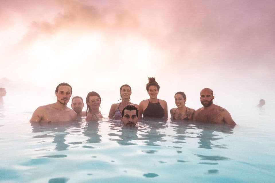 A WeRoad group trip smiles for the camera while bathing together in the steamy, milky-blue water of a geothermal spa.