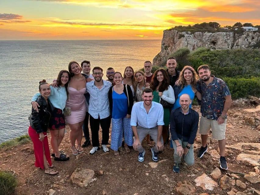 Un voyage de groupe WeRoad posant pour une photo sur une falaise surplombant la mer lors d'un coucher de soleil doré.