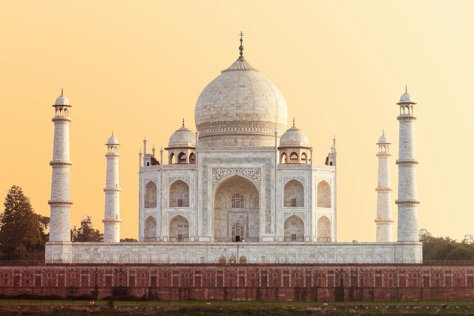 Il Taj Mahal, un mausoleo in marmo bianco avorio, è fotografato frontalmente contro un cielo dorato all'alba.