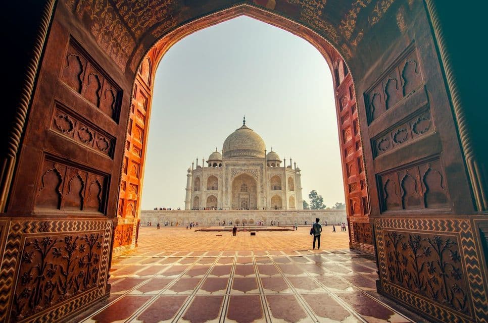 Una vista del Taj Mahal è incorniciata dalle grandi porte aperte di un arco ornato in arenaria rossa e da un cortile piastrellato.