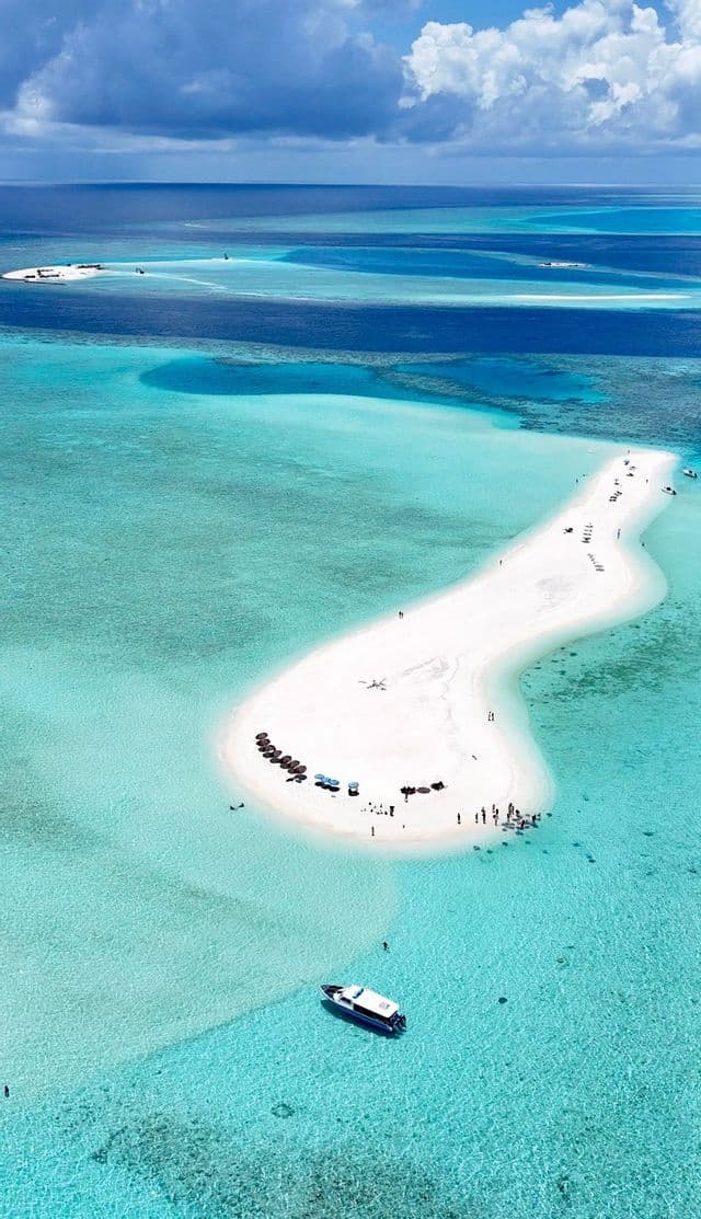 Immagine aerea di un viaggio di gruppo WeRoad su un lungo banco di sabbia bianca in un oceano turchese, con una barca ancorata nell'acqua cristallina.