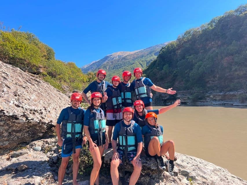 Eine WeRoad-Gruppe posiert mit roten Helmen und Schwimmwesten auf felsigem Boden an einem Fluss in einer Schlucht