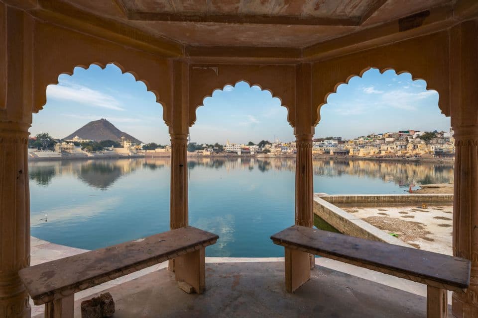 Un pueblo junto al lago y una colina se ven a través de tres arcos de piedra festoneados, con dos bancos de piedra vacíos en primer plano.