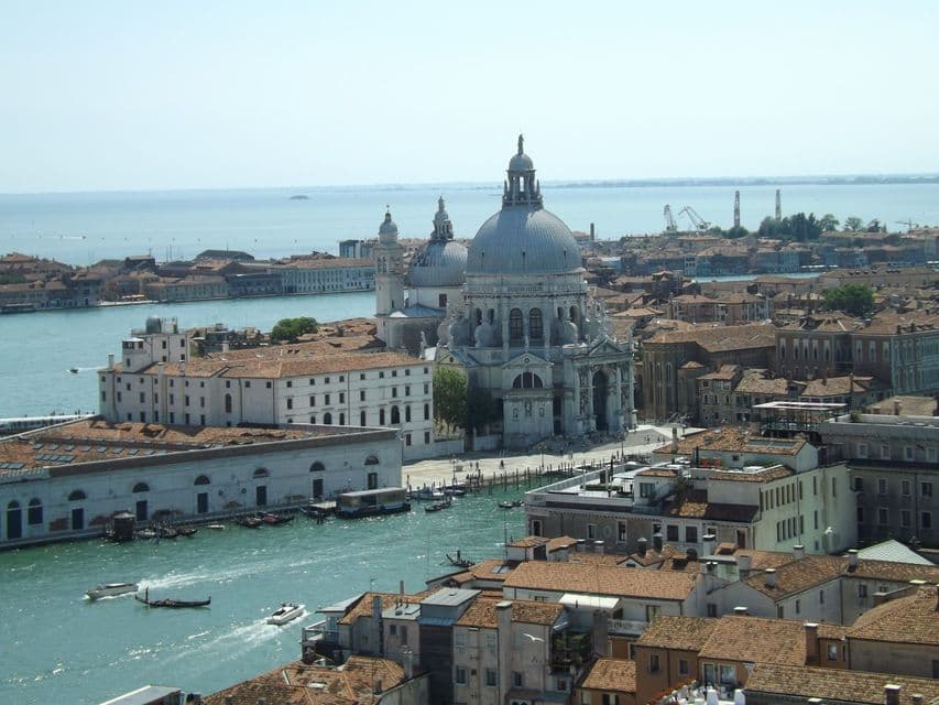 A high-angle view of a historic city's canals, featuring a prominent domed basilica and buildings with terracotta roofs.