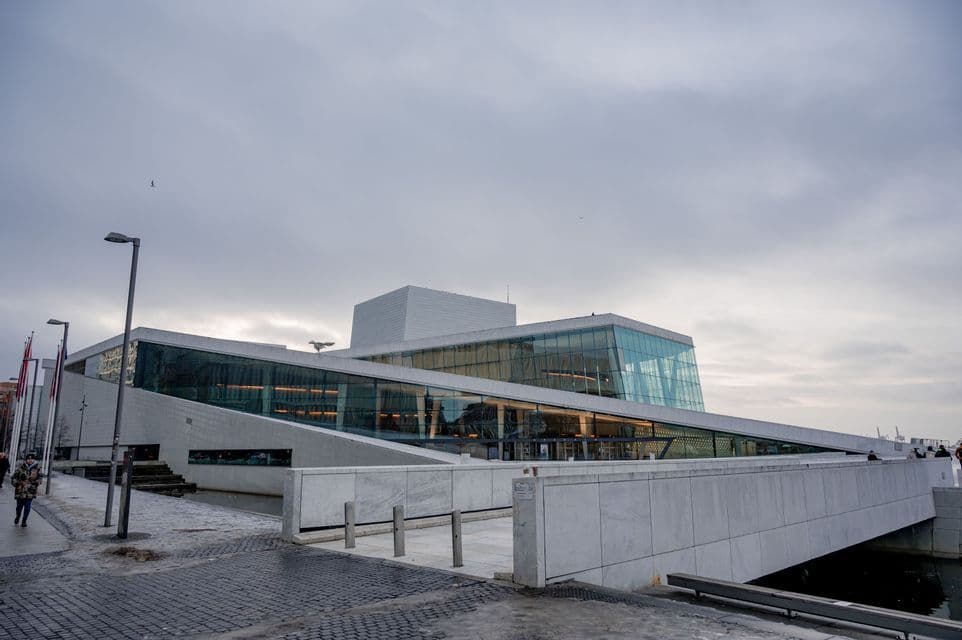 Modern angular building with large glass windows and white stone ramps under an overcast sky.